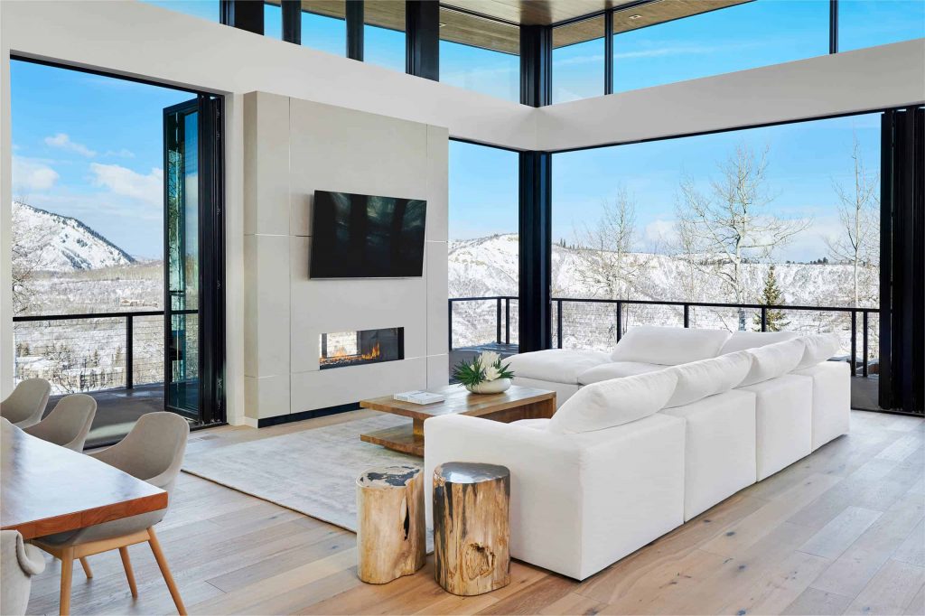 宽敞的现代客厅，带阳台和窗墙，木地板，白墙和沙发，小壁炉和壁炉上方的电视
