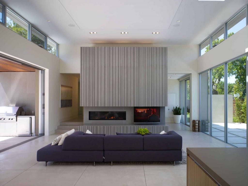 宽敞的客厅灰色瓷砖地板，窗墙，紫色沙发，灰色纹理墙，宽大的壁炉和壁炉旁边的电视